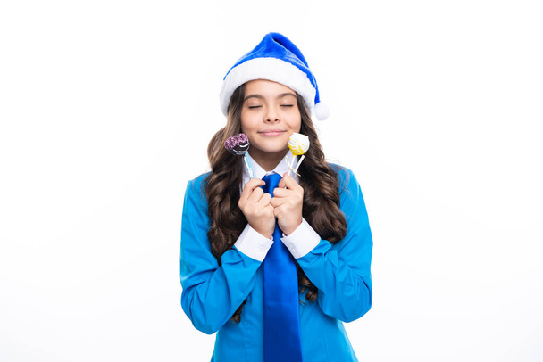 Концепция празднования Рождества и Нового года для детей. Портрет девочка-подросток в синей шляпе Санта-Клауса, рубашке и галстуке провести Рождество конфеты леденец изолирован на белом фоне, скопировать пространство - Фото, изображение