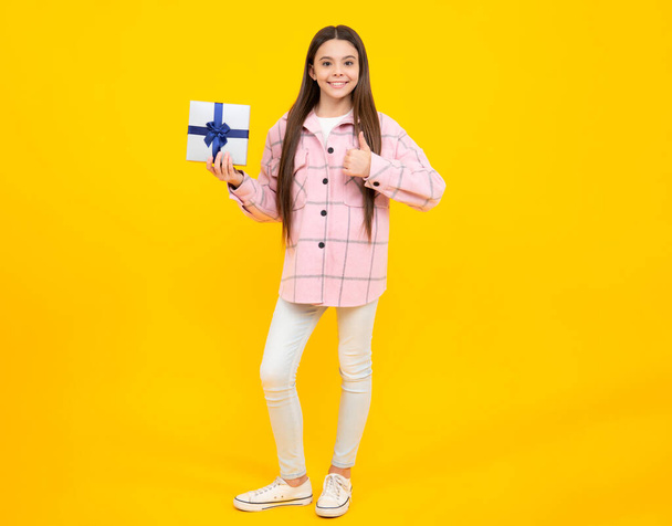 Teenager dítě dívka drží dárek box izolované přes žluté pozadí studia. Přítomen, pozdrav a dar koncept. Narozeninová dovolená koncept - Fotografie, Obrázek