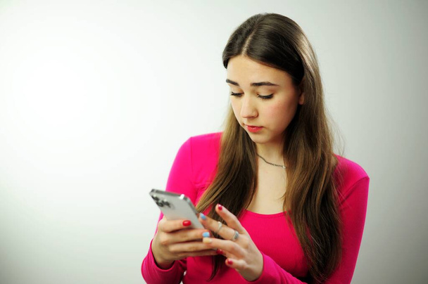 Online learning Social media Instagram tiktok 16-20 years Girl in a pink shirt is playing games on the phone he is smiling and interested on a white background Online life internet school lessons - Fotó, kép