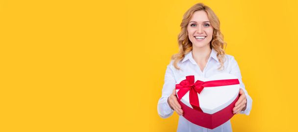 positive woman hold present heart box on yellow background. Woman isolated face portrait, banner with mock up copy space - Фото, зображення