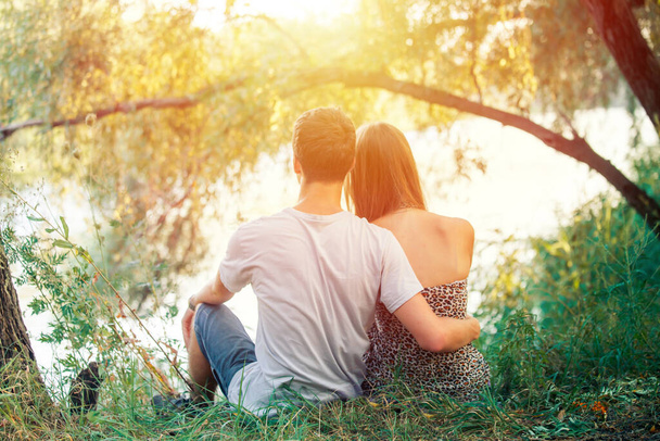 Deux adolescents garçons et filles se tenant la main. Il aime la fille. Les jeunes amants s'assoient sur le bord du lac près de l'arbre. - Photo, image