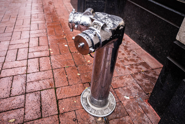 Una boca de incendios de metal en una acera de ladrillo en el barrio de Chinatown en Washington D.C. Tomada en un día lluvioso. - Foto, imagen