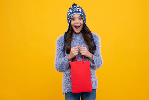 Stylowa nastolatka w zimie ciepły kapelusz z torbami na zakupy. Dzieciak trzyma zakupy. Szczęśliwa twarz, pozytywne i uśmiechnięte emocje nastolatki - Zdjęcie, obraz