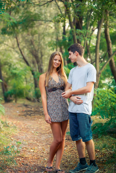 Guy looks at his beloved laughing girl. Caring young man holding the hand of a minor beloved in the park - Photo, Image