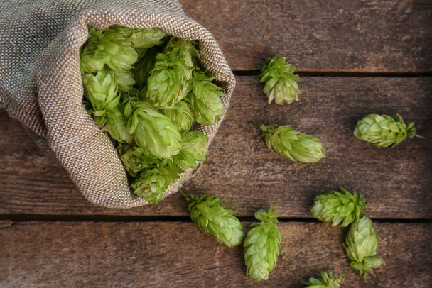 Sack and fresh green hops on wooden table, flat lay - Photo, Image
