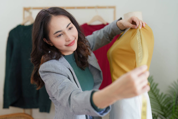 Azjatycka kobieta moda projektant tkaniny krawiec kreatywny pracuje dla nowej kolekcji. Szczęśliwy właściciel sklepu internetowego przygotowuje zamówienie na wysyłkę. - Zdjęcie, obraz