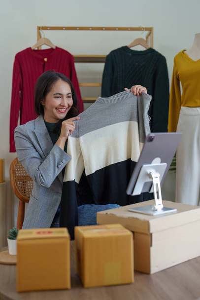 Azjatycka kobieta moda projektant tkaniny krawiec kreatywny pracuje dla nowej kolekcji. Szczęśliwy właściciel sklepu internetowego przygotowuje zamówienie na wysyłkę. - Zdjęcie, obraz