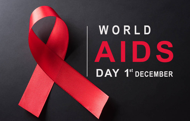 Κλείσιμο της κόκκινης κορδέλας HIV, της παγκόσμιας ημέρας ευαισθητοποίησης για το AIDS και του κειμένου σε μαύρο φόντο. Υγειονομική και ιατρική έννοια. - Φωτογραφία, εικόνα