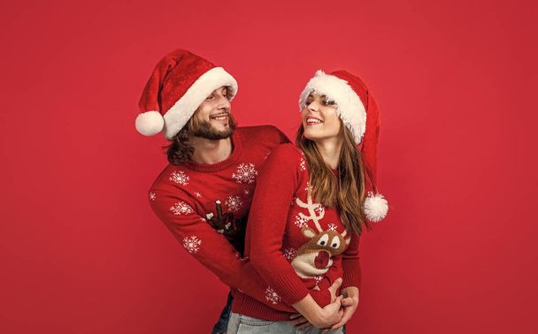 Yılbaşı zamanı. Yeni yıl çifti örgü süveter ve Noel Baba şapkası takıyor. Noel partisi eğlencesi için hazırlan. Genç aile için mutlu tatiller. Kırmızı arka planda kadın ve erkek. Aşk. - Fotoğraf, Görsel