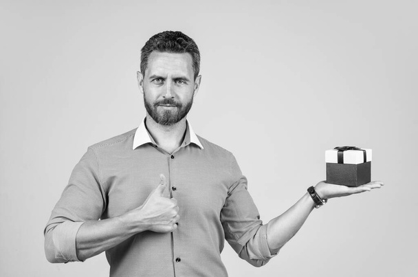 mature confident man businessman in shirt presenting gift box and showing thumb up, shopping sale. - 写真・画像