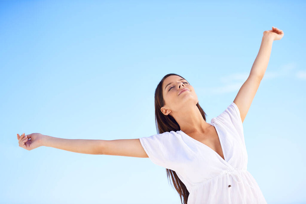 Całkowicie wolna... beztroska młoda kobieta stojąca z ramionami wyciągniętymi na błękitne niebo - Zdjęcie, obraz