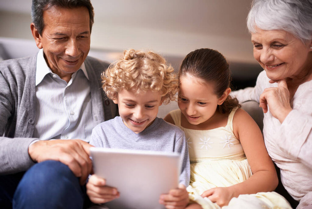 おばあちゃんを表示し、最新の技術を把握.ソファに座っている間にデジタルタブレットを使用して2人の子供とその祖父母のショット - 写真・画像