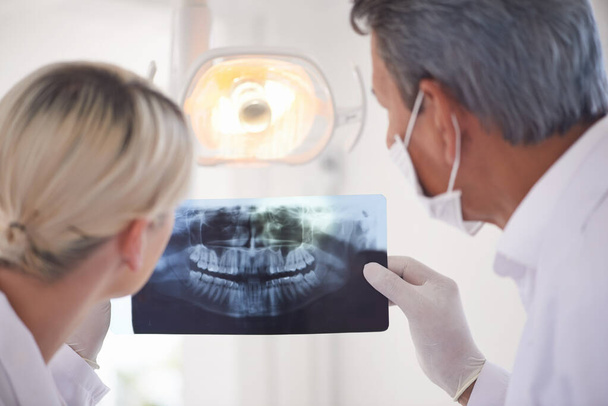 Ik bekijk de röntgenfoto 's. Achteraanzicht foto van een tandarts en zijn assistent op zoek naar een röntgenfoto - Foto, afbeelding
