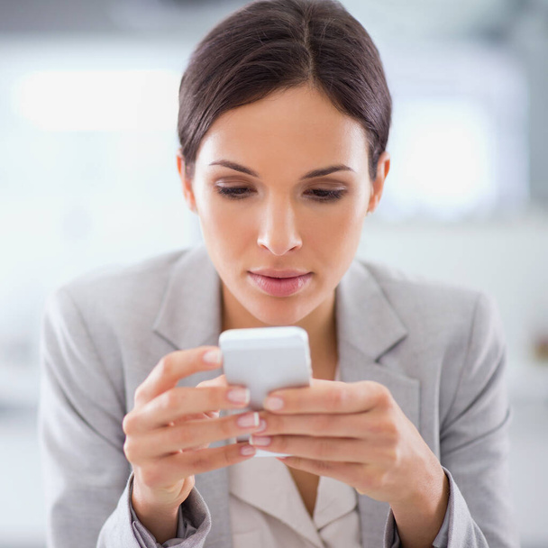 A text a day keeps the motivation alive. a woman using a cellphone while sitting at a desk in an office - Foto, afbeelding