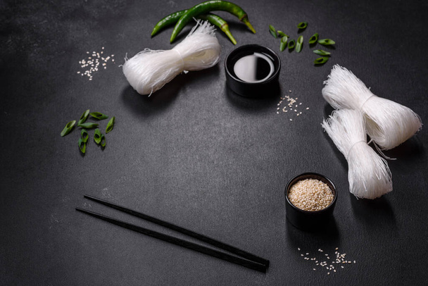 Tasty dish of Asian cuisine with rice noodles, chicken, asparagus, pepper, sesame seeds and soy sauce on dark concrete background - Zdjęcie, obraz