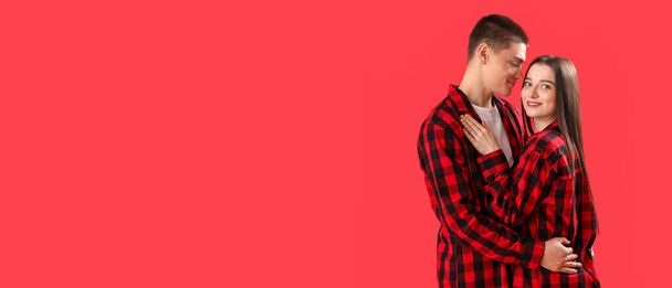 Happy young couple in checkered Christmas pajamas on red background with space for text - Fotografie, Obrázek