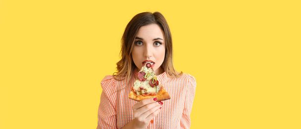 Portrait of beautiful young woman eating yummy pizza on yellow background - Foto, Imagen