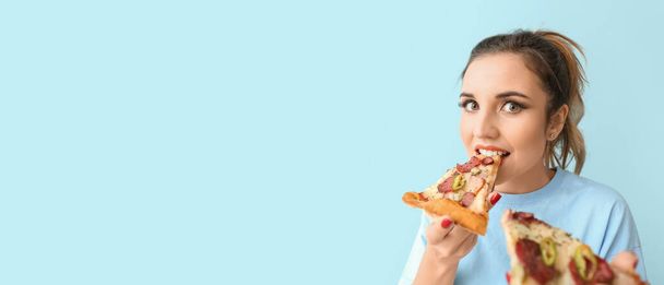Portrait of beautiful young woman eating tasty pizza on light blue background with space for text - Photo, Image