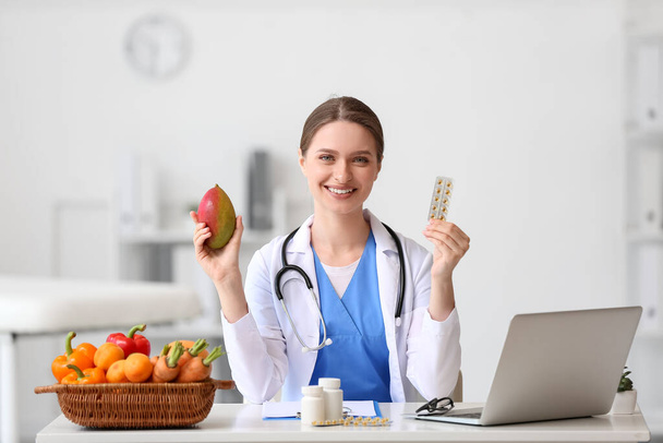 Γυναίκα γιατρός με βιταμίνες και μάνγκο κάθεται στο τραπέζι στην κλινική - Φωτογραφία, εικόνα