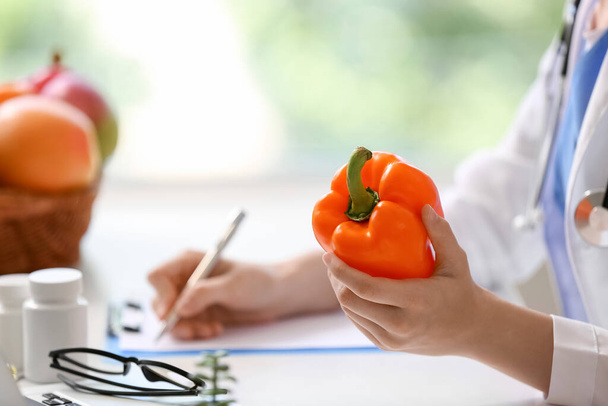 Female doctor with bell pepper writing in clipboard at hospital, closeup - Фото, изображение