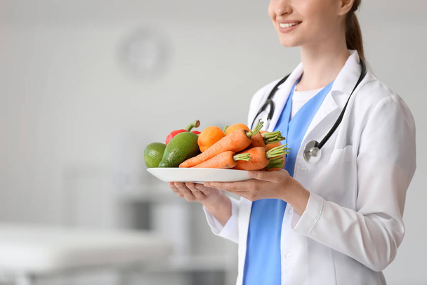 Female doctor with plate of vegetables in clinic - Photo, Image