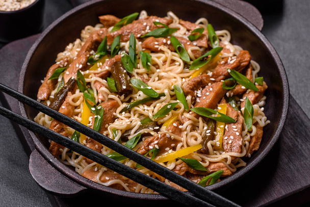Chutné jídlo asijské kuchyně s rýžovými nudlemi, kuřecím masem, chřestem, pepřem, sezamovými semínky a sójovou omáčkou na tmavém betonovém pozadí - Fotografie, Obrázek
