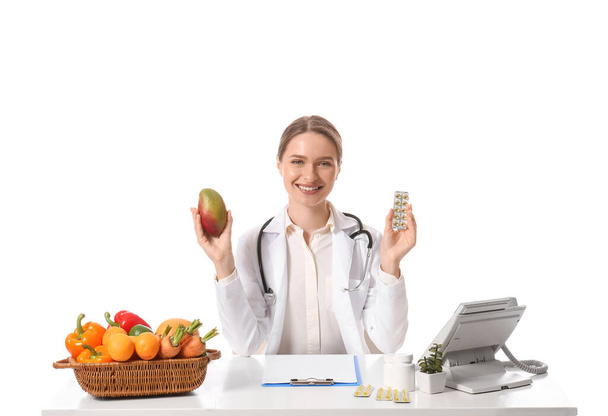 Женщина-врач с витаминами и овощами за столом на белом фоне - Фото, изображение