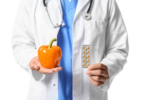 Male doctor with vitamins and bell pepper on white background, closeup - Fotó, kép