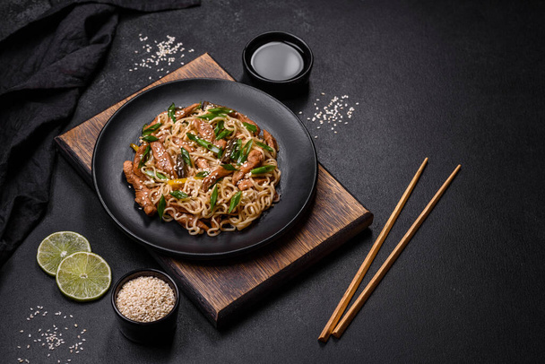 Ízletes étel ázsiai konyha rizs tészta, csirke, spárga, bors, szezámmag és szójaszósz sötét beton alapon - Fotó, kép