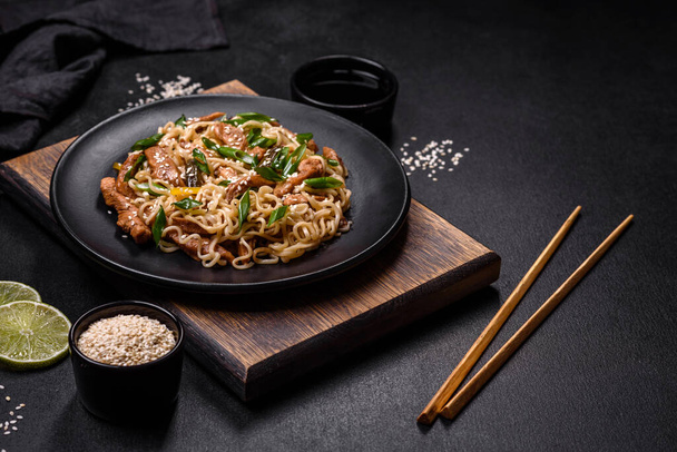 Sabroso plato de cocina asiática con fideos de arroz, pollo, espárragos, pimienta, semillas de sésamo y salsa de soja sobre fondo de hormigón oscuro - Foto, imagen