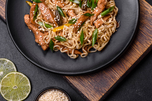 Tasty dish of Asian cuisine with rice noodles, chicken, asparagus, pepper, sesame seeds and soy sauce on dark concrete background - Foto, immagini