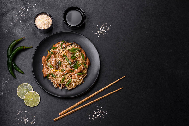 Вкусное блюдо азиатской кухни с рисовой лапшой, курицей, спаржей, перцем, кунжутом и соевым соусом на темно-бетонном фоне - Фото, изображение