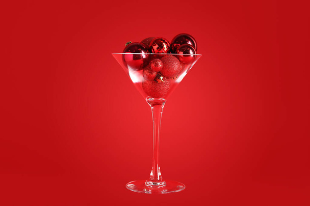 Glass with Christmas balls on red background - Fotó, kép
