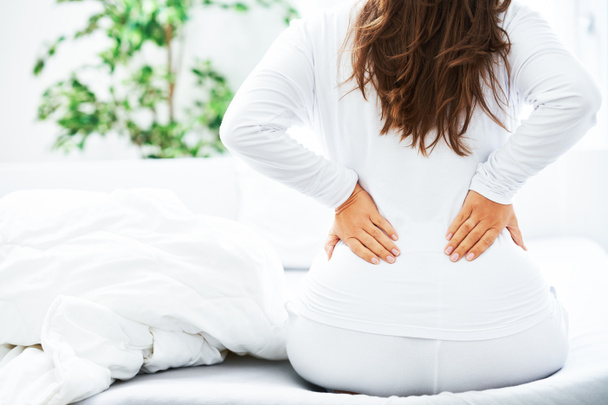 Jeune femme brune essuie son problème de dos dans le lit. Photo de haute qualité - Photo, image