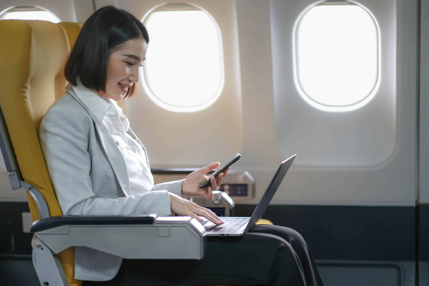 Ázsiai nő utas ül a repülőgépen az ablak közelében, és olvasás híreket a társadalmi hálózatok vagy az utazási alkalmazások okostelefon. - Fotó, kép