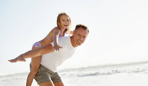 Amusez-vous à la plage avec papa. une jeune fille sur ses pères de retour à la plage - Photo, image