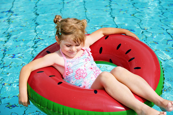 Happy little girl playing with colorful inflatable ring in outdoor swimming pool on sunny summer day. Preschool child learn to swim. Summer outdoor activity. - Photo, Image