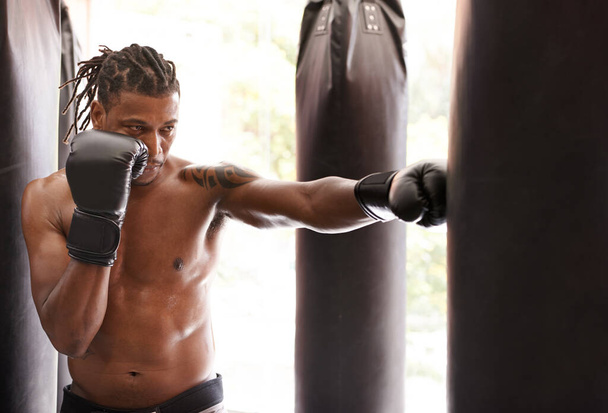 Dejando todo fuera. un joven boxeador practicando en un saco de boxeo en un gimnasio - Foto, imagen