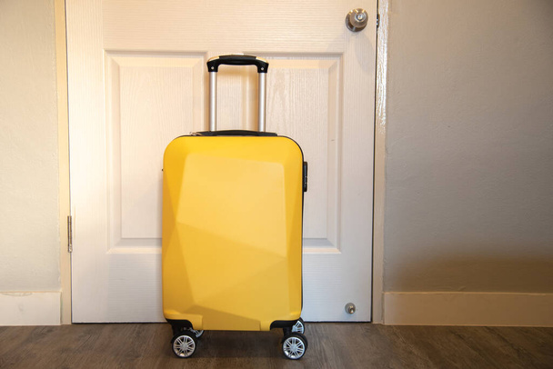Gele reiskoffer in de slaapkamer op de achtergrond van de deur - ontspannen tijd, vakantie, weekend en reisconcept. - Foto, afbeelding