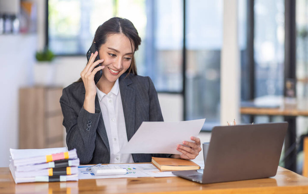 Asian female business analyst financial advisor call phone and preparing statistic report studying documents on work desk, Asian business woman work with documents in the office. - Foto, Imagen