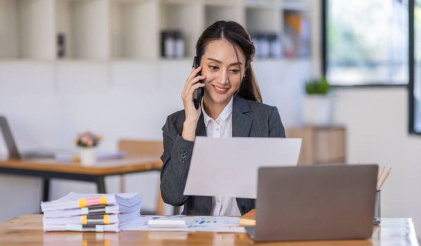 Asian female business analyst financial advisor call phone and preparing statistic report studying documents on work desk, Asian business woman work with documents in the office. - Foto, imagen