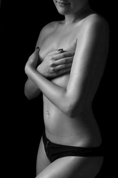jovem mulher esbelta posando topless em um fundo preto - Foto, Imagem