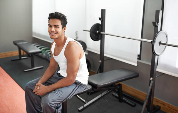 This is going to be an awesome workout. A young ethnic man sitting on a weight bench at a gym - Photo, image