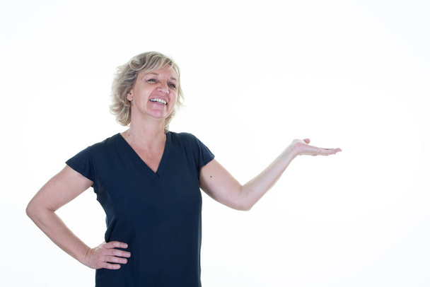 senior woman shows object promo deal smiles positively points at copy space white background - Photo, Image