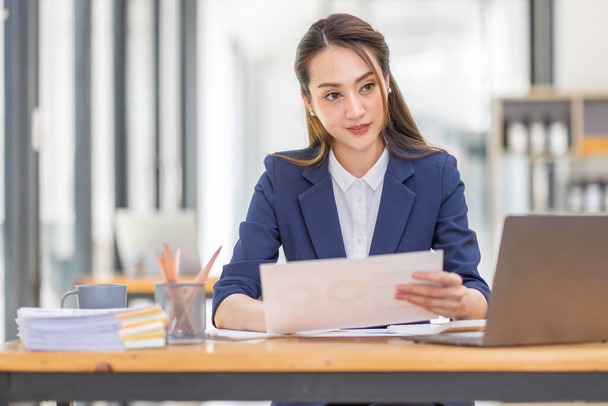 Cabelo castanho vestindo casaco azul claro sorrindo mulher asiática trabalho com laptop documento no escritório, fazendo planejamento analisando o relatório financeiro, investimento em plano de negócios, conceito de análise financeira. - Foto, Imagem