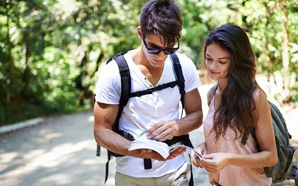 Which way should we go. a young couple looking at a guidebook while out hiking - Foto, Imagen