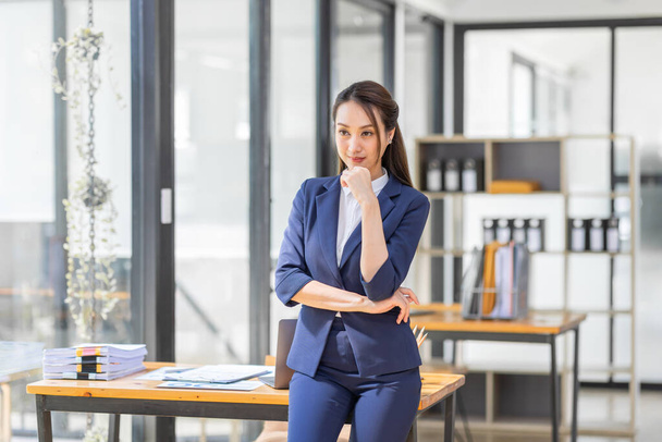 Portrait of young Asian woman hoding coffee cup and standing in a busy modern workplace - 写真・画像