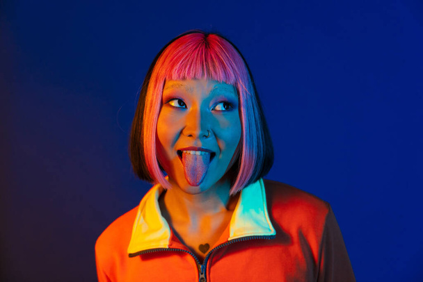 Asian girl with pink hair and piercing showing her tongue isolated over blue background - Fotografie, Obrázek