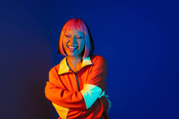 Asian girl with pink hair and piercing showing her tongue isolated over blue background - Photo, image