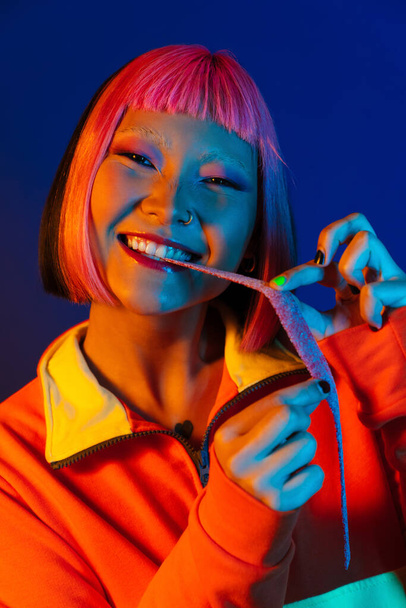 Asian girl with pink hair making fun while eating chewing marmalade isolated over blue background - Foto, immagini